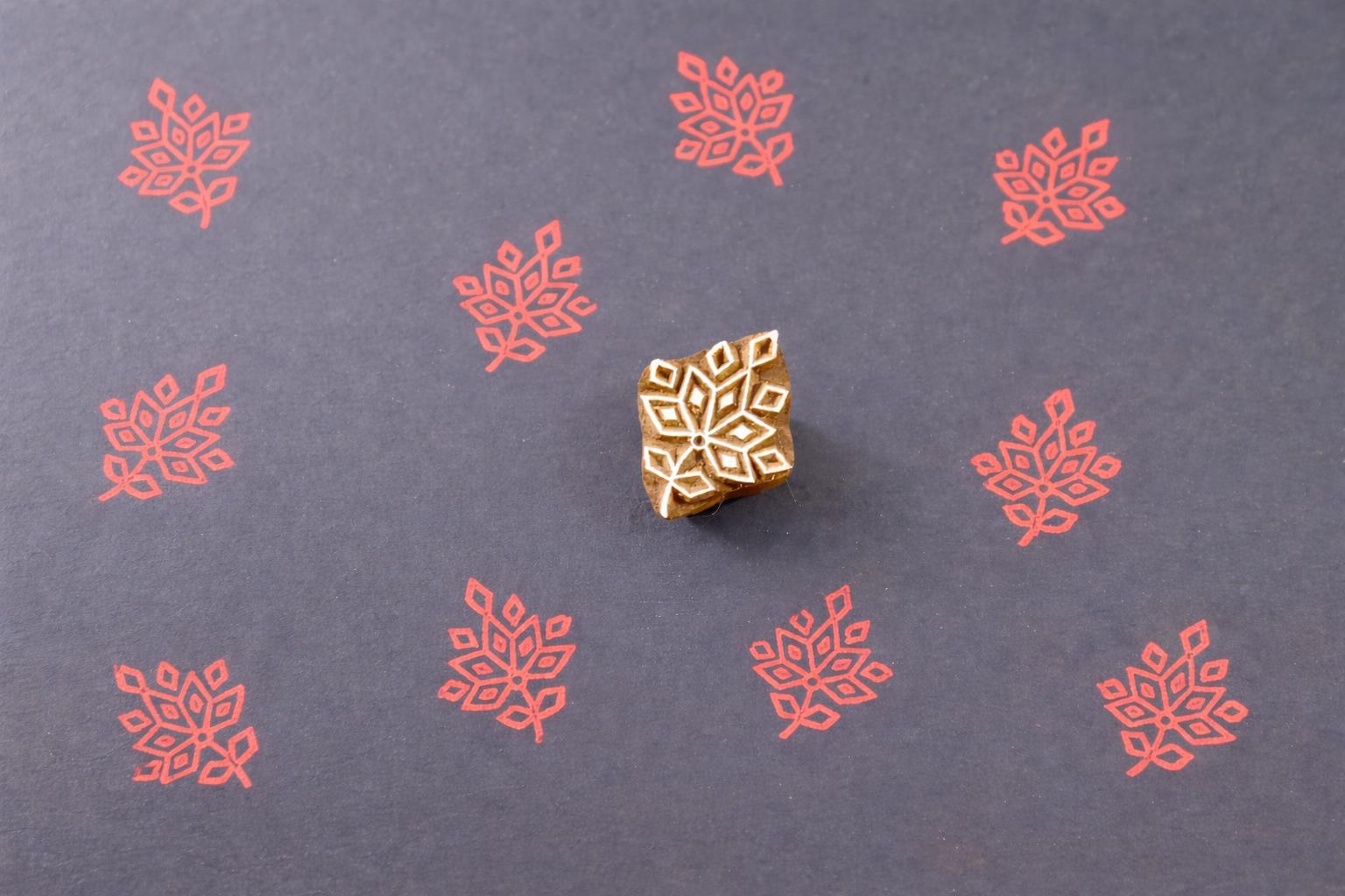 Wooden block printing stamp creating red leaf pattern prints on dark blue paper.