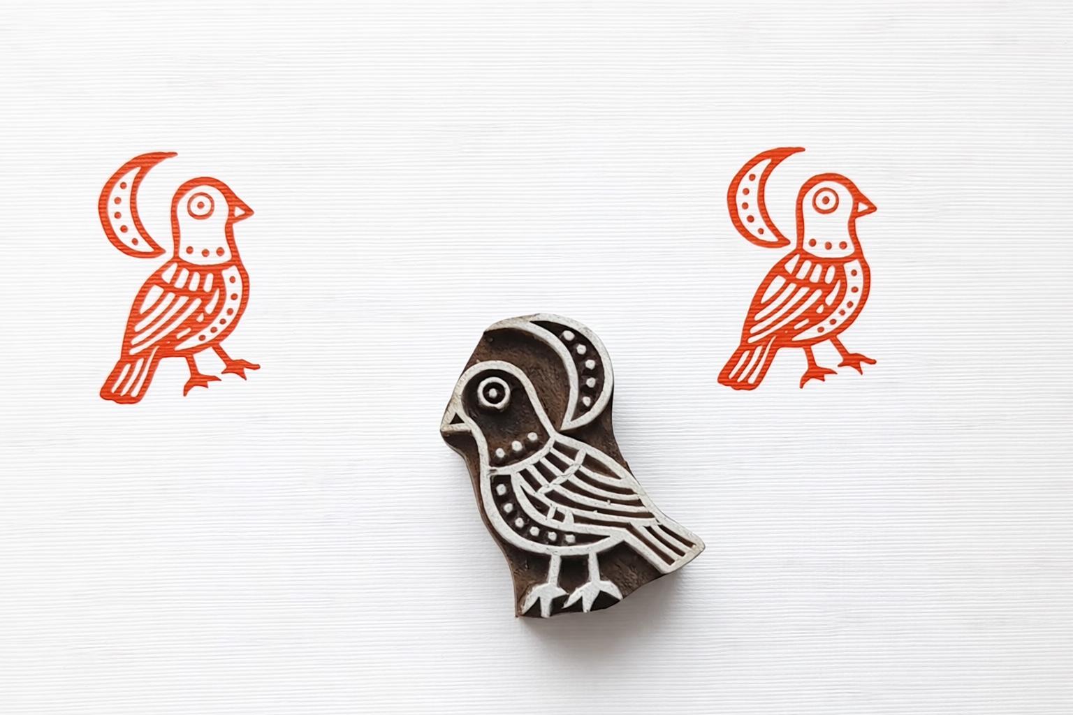 Hand carved wooden bird block printing stamp with two orange bird prints on white paper.