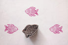 Hand carved wooden fish block printing stamp creating pink fish prints on white textured paper.