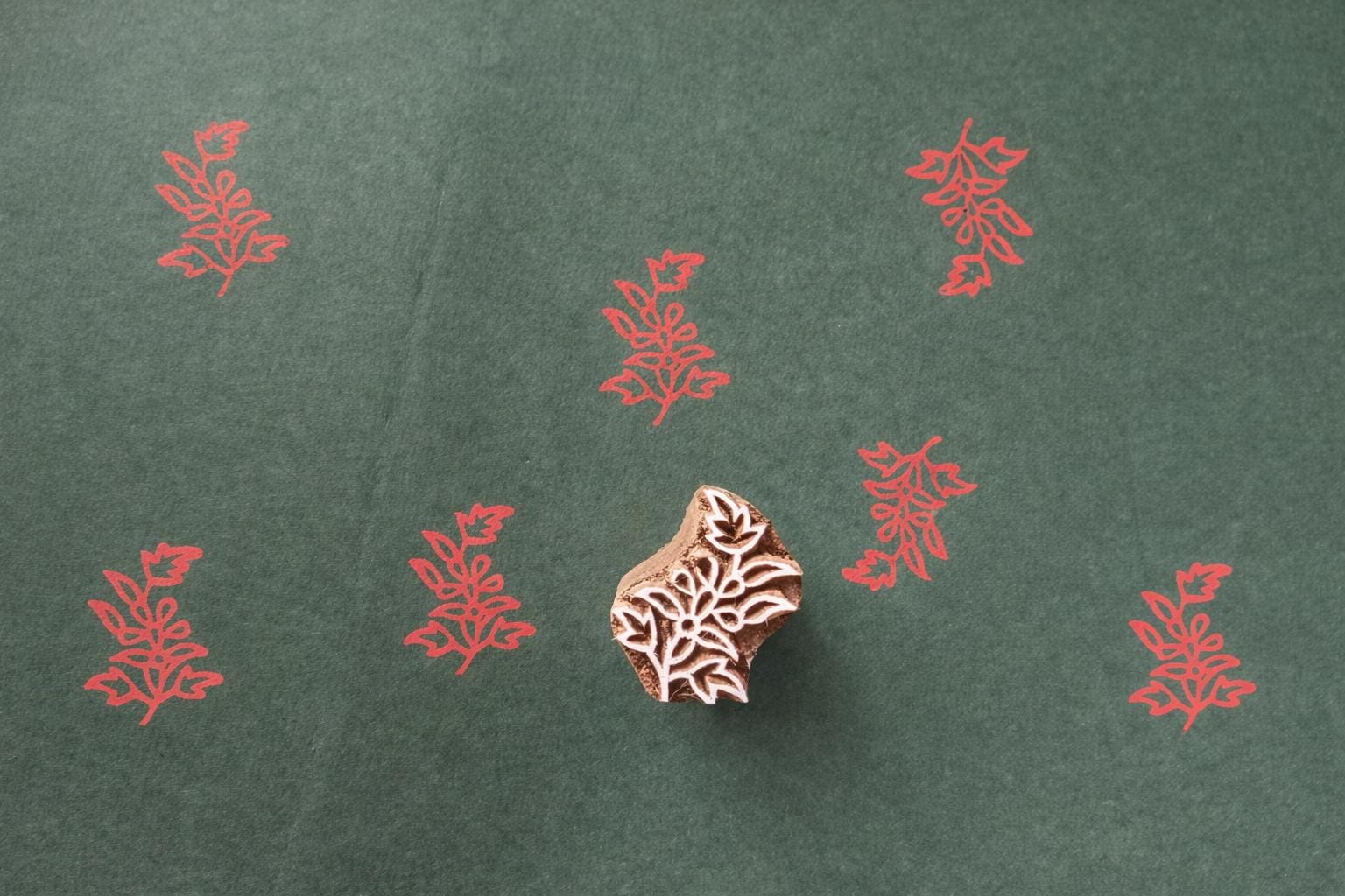 Hand carved wooden floral block printing stamp producing red plant motif prints on dark green paper.