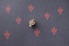 Wooden block printing stamp creating small red floral pattern prints on dark charcoal black paper.