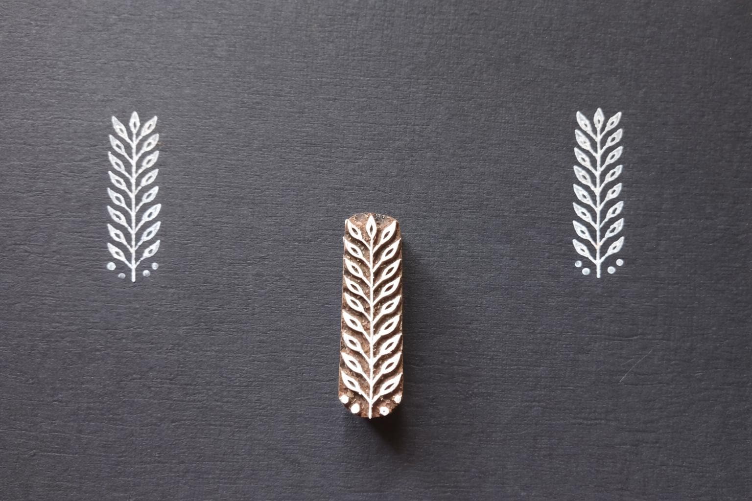 Hand carved leaf textile stamp made from wood showing white leaf prints on dark paper.