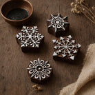 Set of four hand carved wooden geometric snowflake block printing stamps displayed on rustic wooden background.
