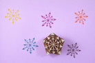 Hand carved wooden arrow snowflake block printing stamp creating colorful geometric snowflake prints on pastel background.