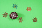Hand carved wooden starburst mandala block printing stamp shown with multicolor star prints on green background.