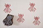 Hand carved wooden fly block printing stamp creating red insect prints on cream paper.