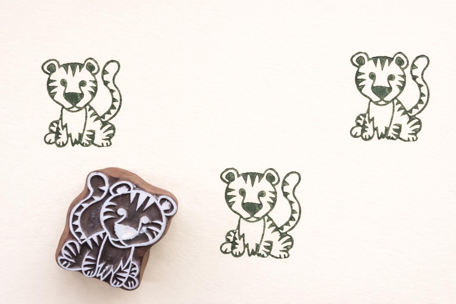 Hand carved wooden tiger cub block printing stamp creating green tiger prints on white paper.