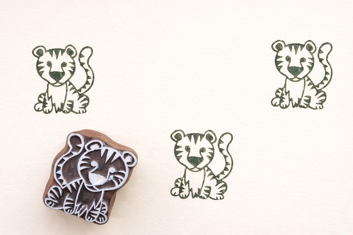 Hand carved wooden tiger cub block printing stamp creating green tiger prints on white paper.