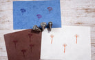 Three hand carved wooden wildflower block printing stamps displayed with printed botanical patterns on blue, brown and white paper.