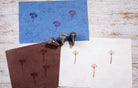 Three hand carved wooden wildflower block printing stamps displayed with printed botanical patterns on blue, brown and white paper.