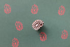 Paisley bloom wooden block printing stamp creating red prints on green handmade paper.
