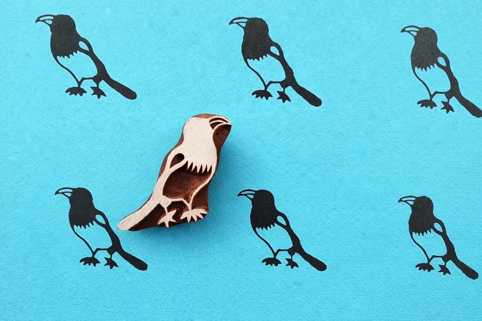 Folk Crow wooden block printing stamp creating black bird prints on bright blue handmade paper.