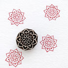 Circular mandala wooden block printing stamp creating red mandala prints on white fabric paper.