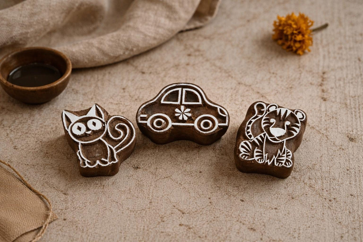 Set of three hand carved wooden kids block printing stamps featuring cute kitten, tiger cub and small car on neutral fabric background.