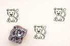 Hand carved wooden tiger cub block printing stamp creating green tiger prints on white paper.