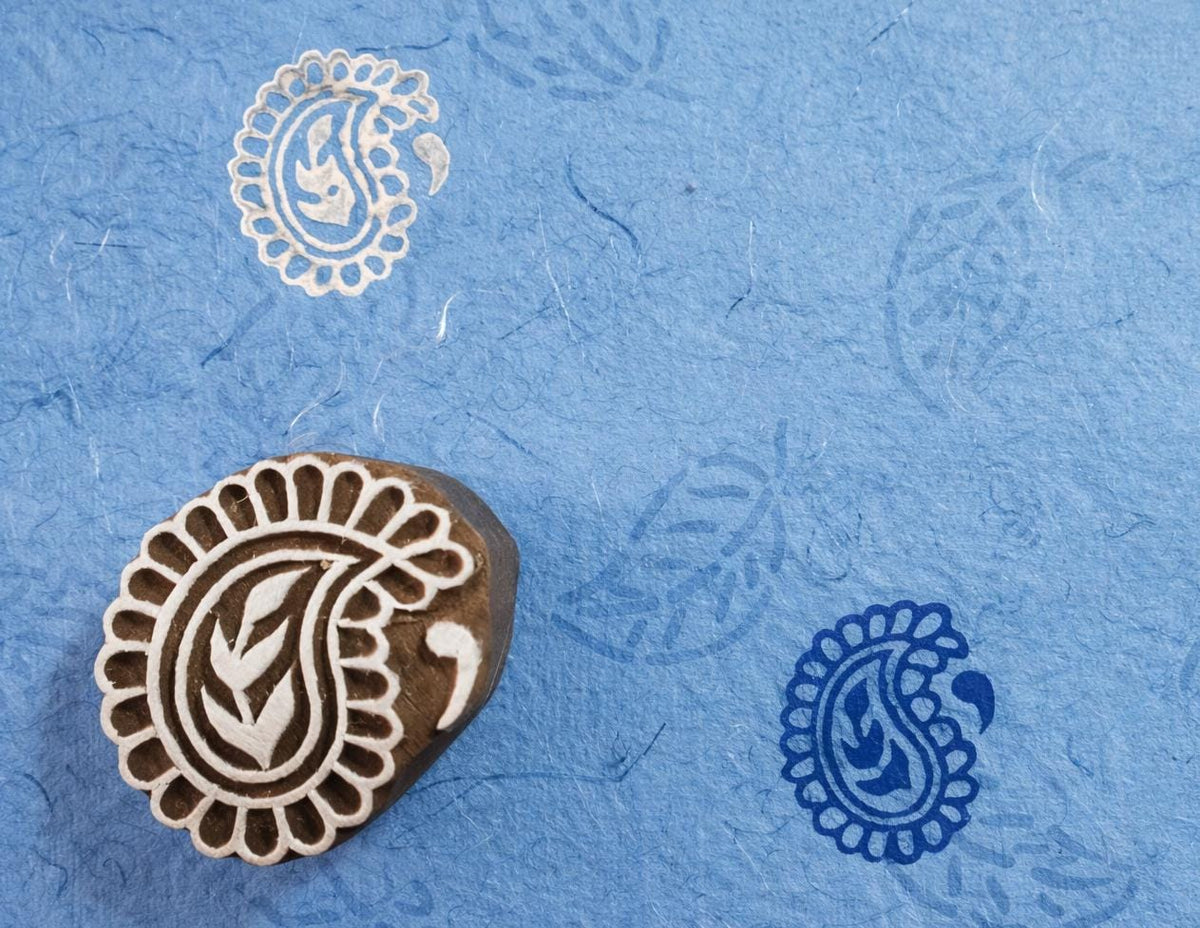 Hand carved large paisley wooden stamp creating white and blue paisley prints on textured paper.