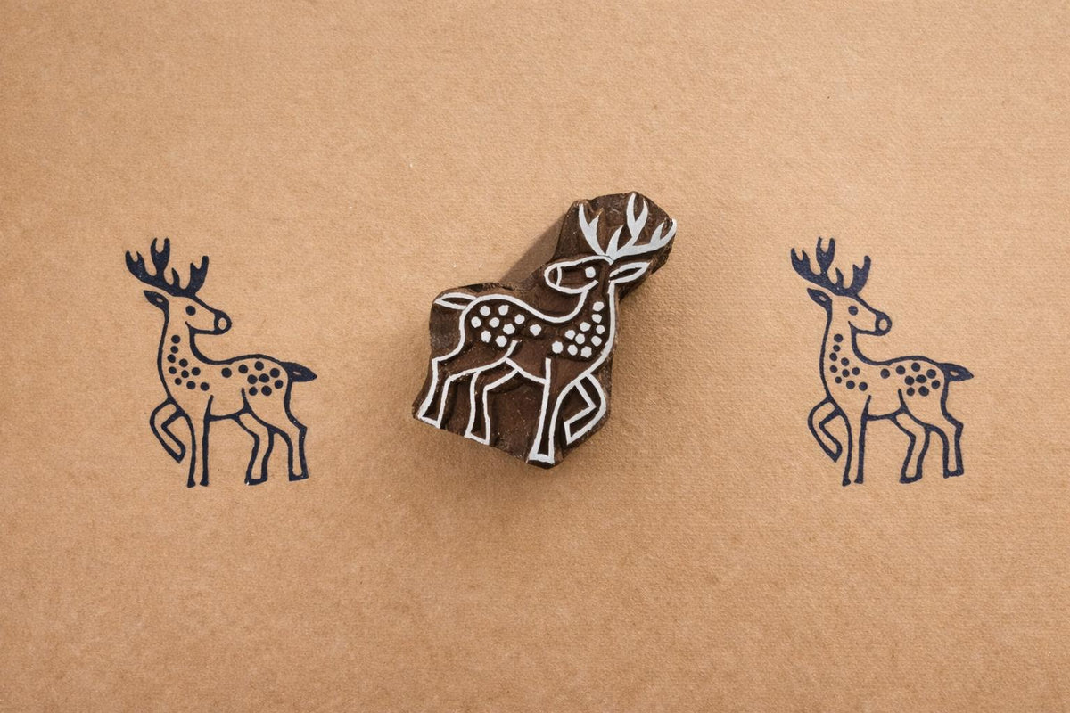 Hand carved wooden deer block printing stamp creating navy blue deer prints on kraft paper.