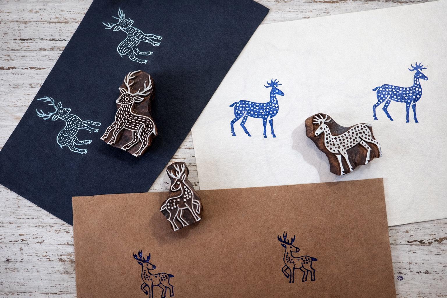 Three wooden deer block printing stamps with printed deer patterns on white, black, and kraft paper.