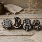 Set of four hand carved wooden block printing stamps with mandala, crescent moon, dreamcatcher and star designs on rustic wooden table.