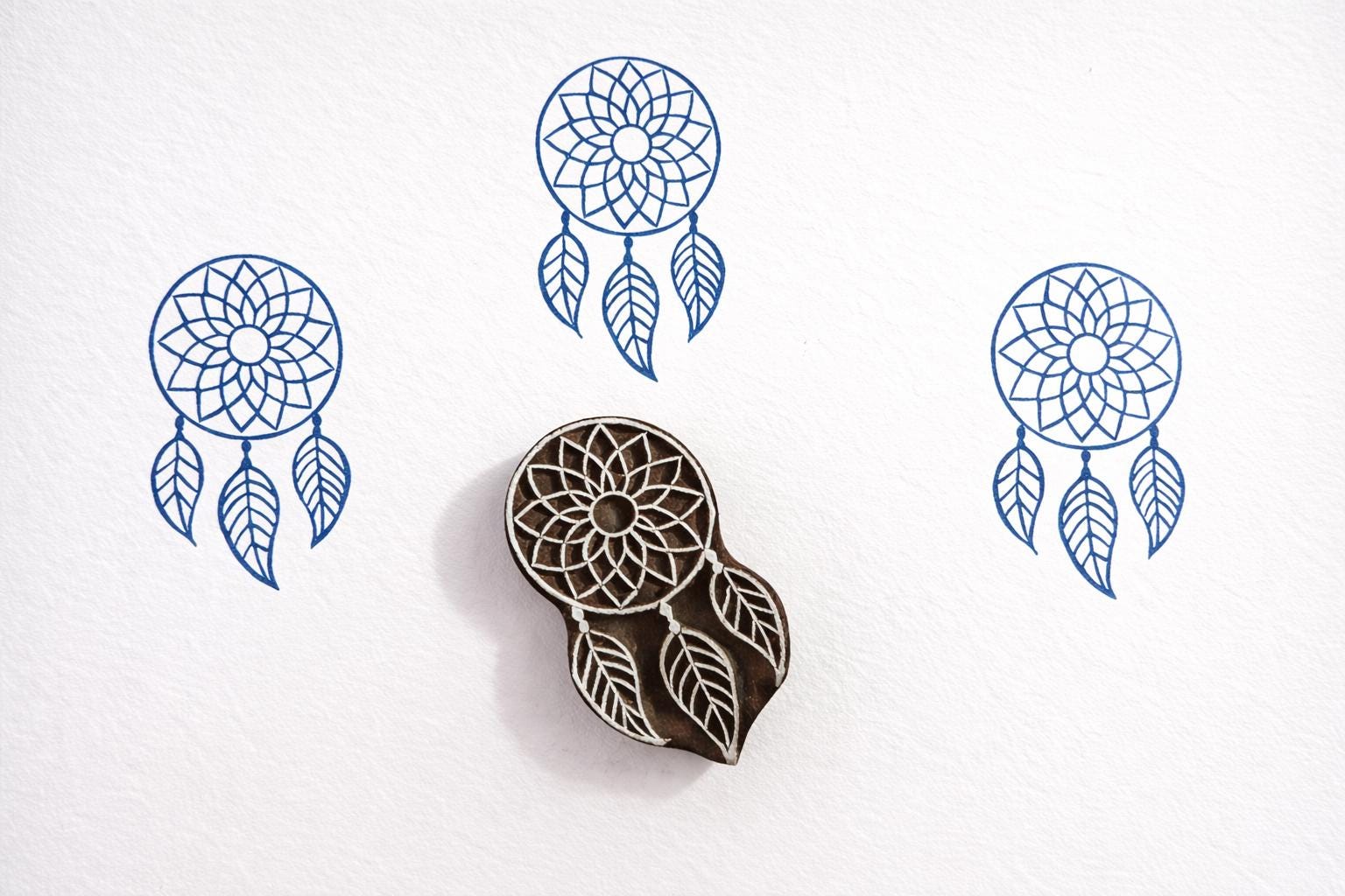 Hand carved wooden dreamcatcher block printing stamp creating blue dreamcatcher prints on white paper.
