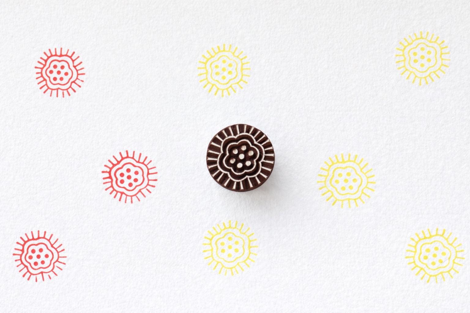 Wooden sun rosette block printing stamp making red and yellow sun prints on white paper.