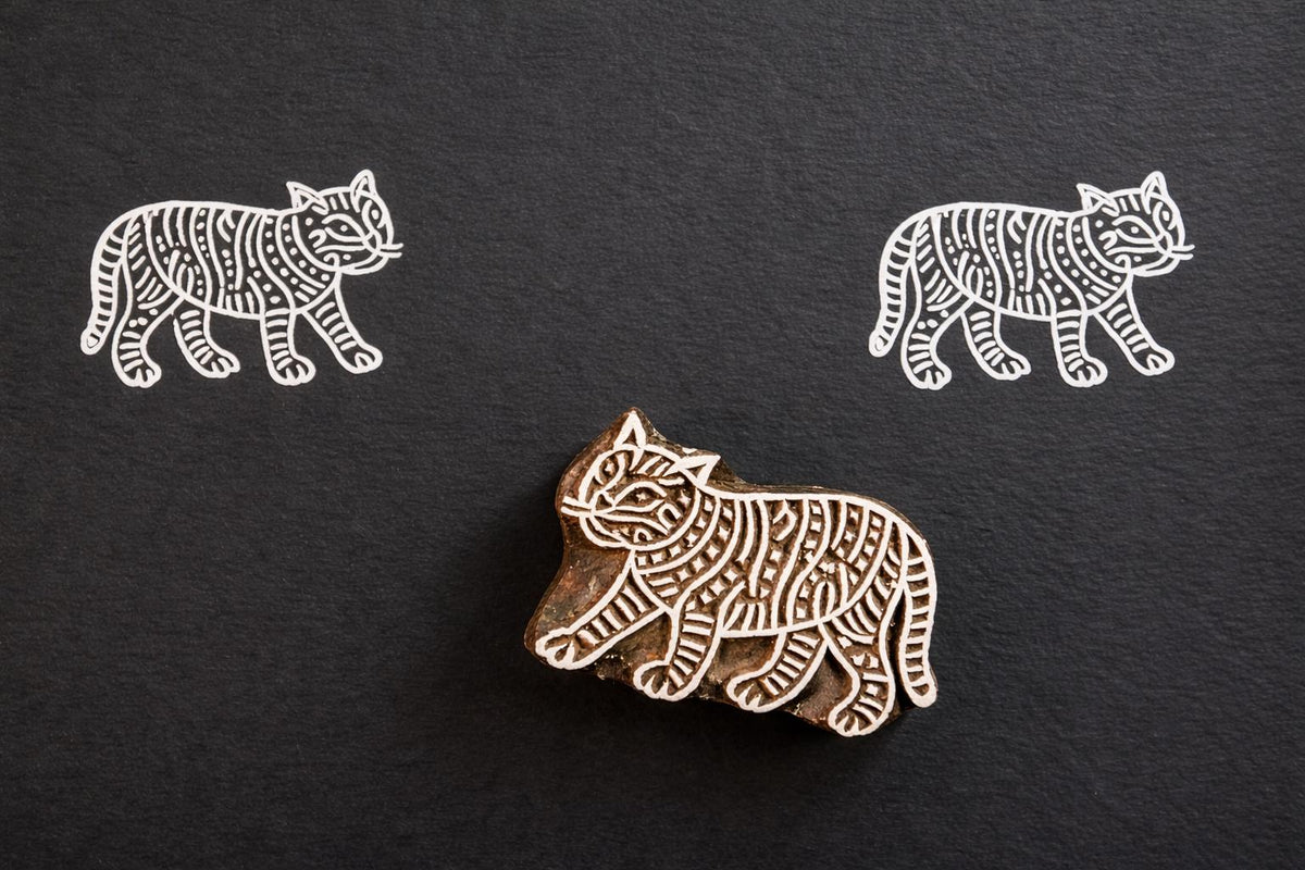 Hand carved wooden striped tiger block printing stamp creating white tiger prints on dark paper.