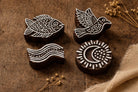 Hand carved wooden block printing stamps featuring bird, fish, moon and wave designs on rustic wooden table.