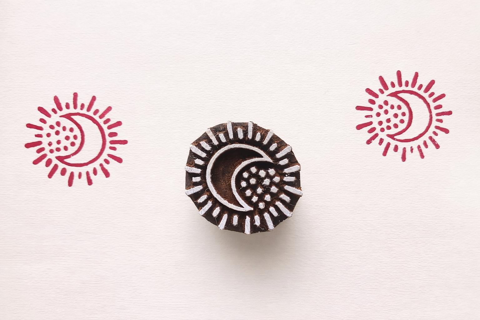 Hand carved wooden crescent moon block printing stamp creating red moon sun prints on white paper.