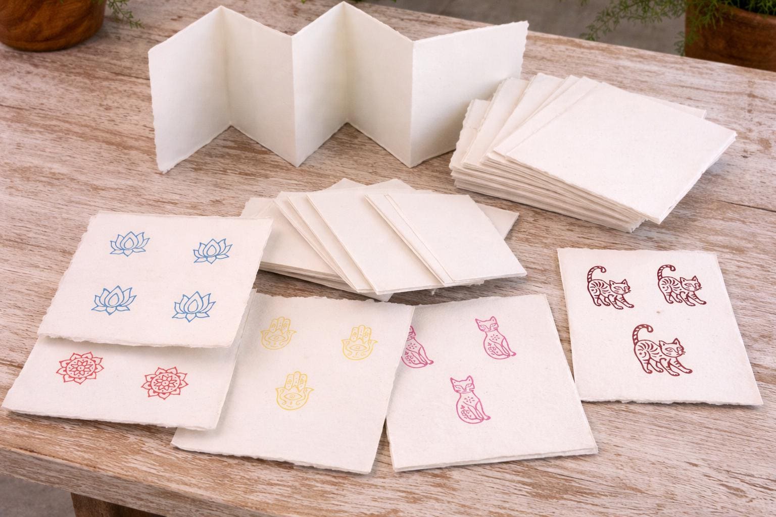 Hand block printed designs in blue, red, yellow, and brown ink on off-white handmade deckle edge paper sheets, showing how the cream paper absorbs print ink beautifully
