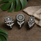 Three hand carved wooden floral block printing stamps featuring lotus and sunflower designs on a rustic wooden table.