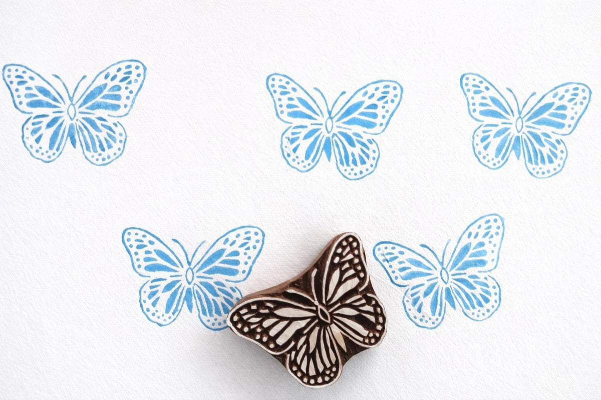 Blue butterfly block print pattern on white handmade paper using wild meadow butterfly wooden stamp, repeated print design showing clean crisp impressions