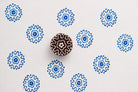 Round sunburst rosette block printing stamp creating blue floral prints on white paper background.