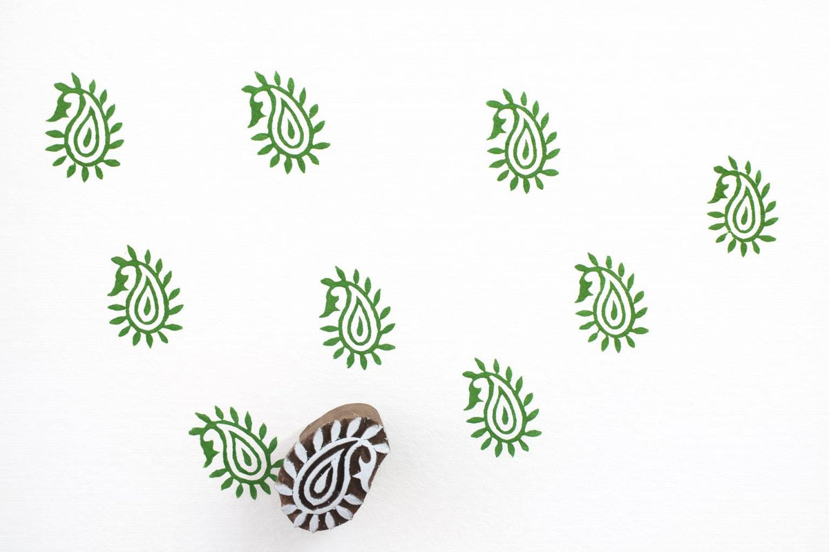 Leaf style paisley wooden block stamp creating green repeat prints on white paper.