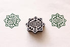 Hand carved wooden Sri Yantra block printing stamp creating green sacred geometry prints on textured paper.