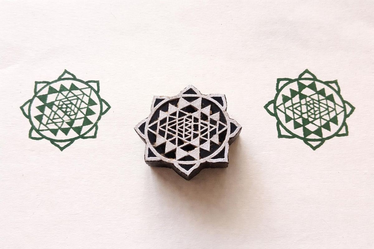 Hand carved wooden Sri Yantra block printing stamp creating green sacred geometry prints on textured paper.