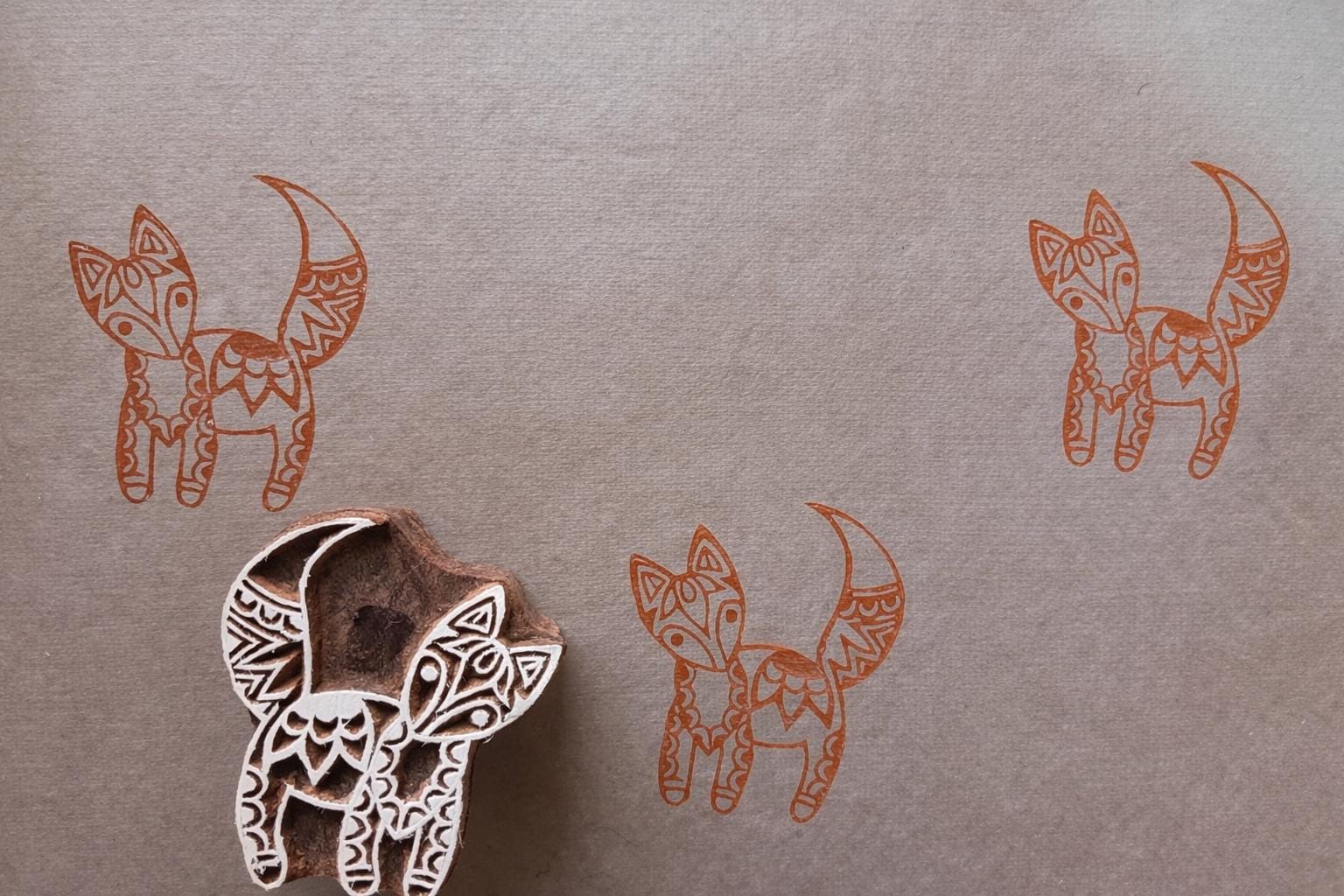Hand-carved wooden fox block stamp with orange fox prints on fabric, featuring a folk art style design