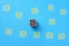 Wooden spiral square block printing stamp making yellow spiral prints on blue paper.