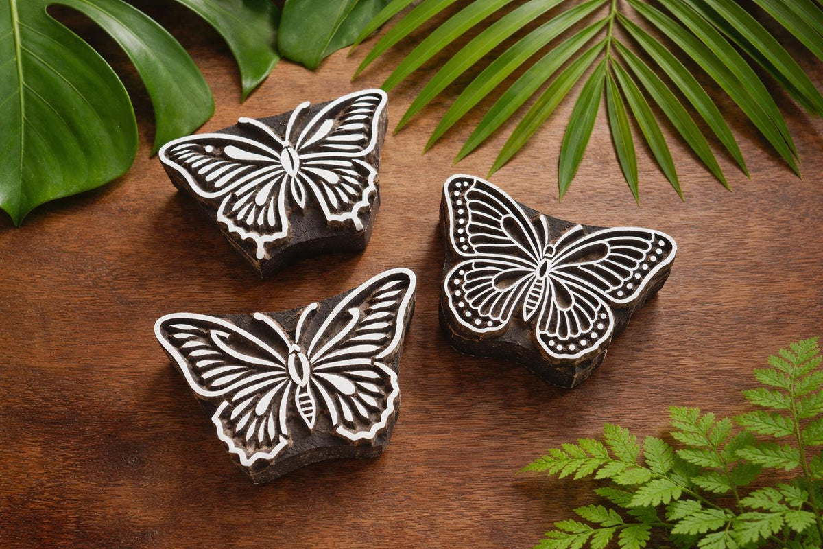 Set of three hand-carved wooden butterfly block stamps with intricate wing patterns on rustic background