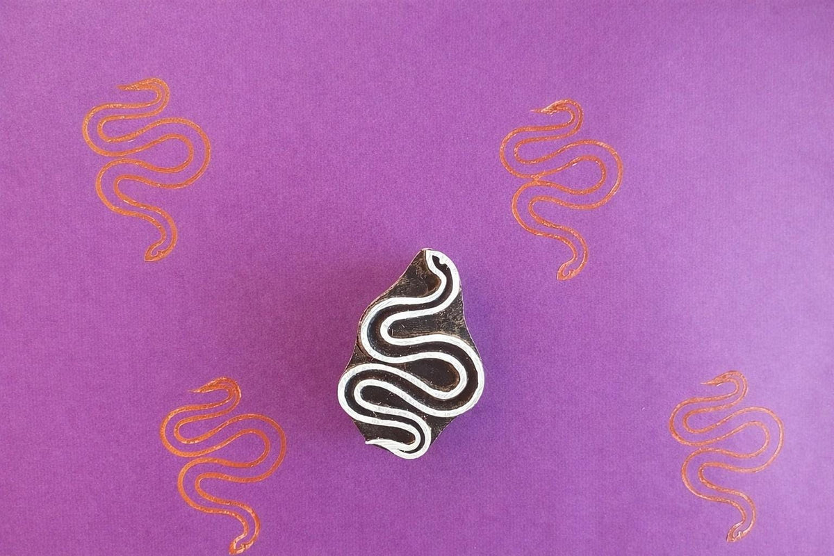 Wooden snake block stamp with flowing serpent design and orange prints on purple background