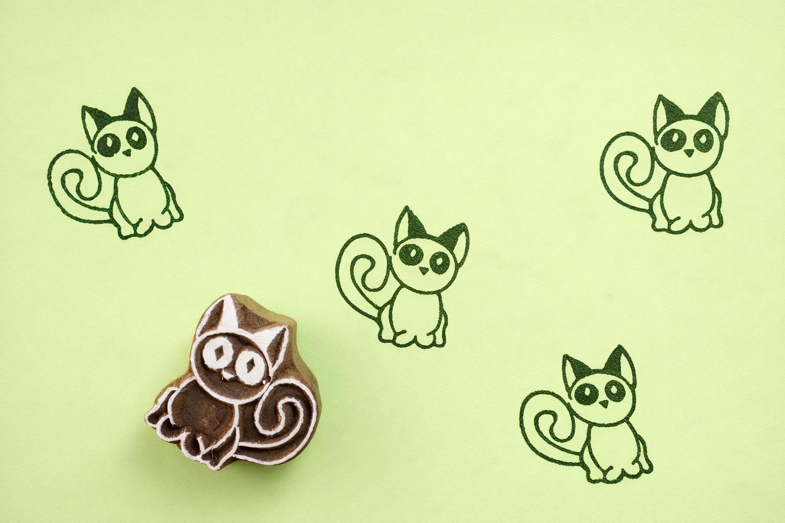 Hand carved wooden kitten block printing stamp creating green cat prints on green paper.