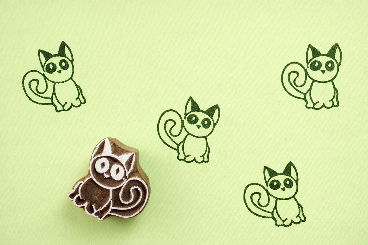 Hand carved wooden kitten block printing stamp creating green cat prints on green paper.