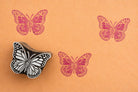 ornate butterfly stamp with pink ink prints on orange background