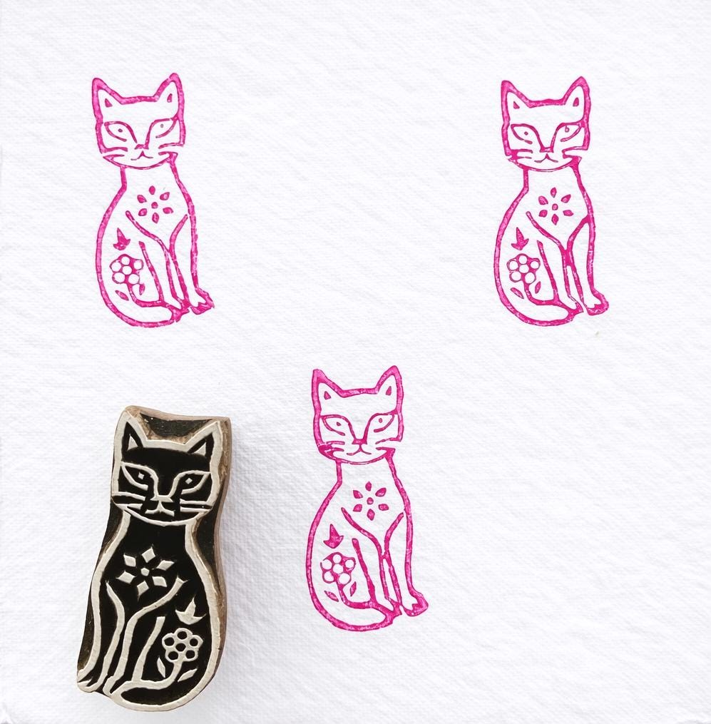 Garden cat wooden block printing stamp with floral motif creating bright pink cat prints on white fabric paper.