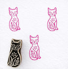 Garden cat wooden block printing stamp with floral motif creating bright pink cat prints on white fabric paper.