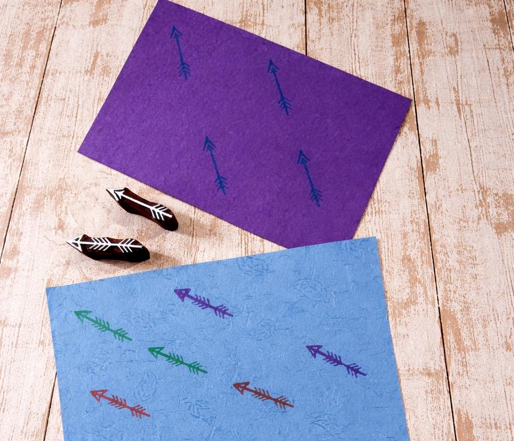 Hand carved arrow stamps with printed arrow patterns on purple and blue handmade paper.
