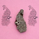 Hand carved wooden block stamp of a detailed peacock with feather pattern printed in black on pink paper