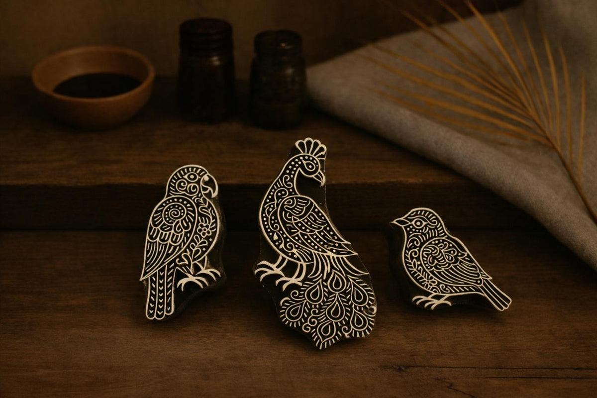 Set of three hand carved wooden block stamps featuring a parrot, peacock, and small bird on a rustic wooden surface