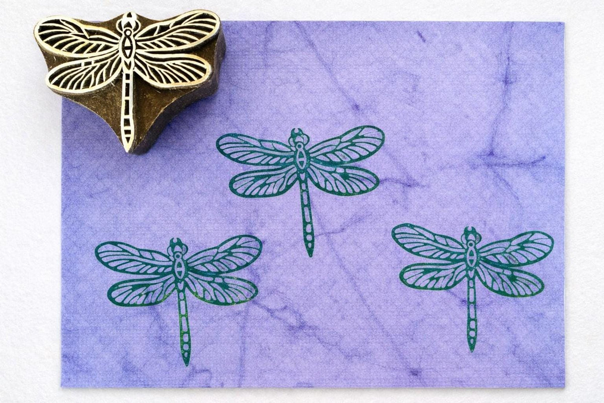 Hand carved wooden dragonfly stamp creating a simple winged dragonfly pattern printed in green ink on purple paper