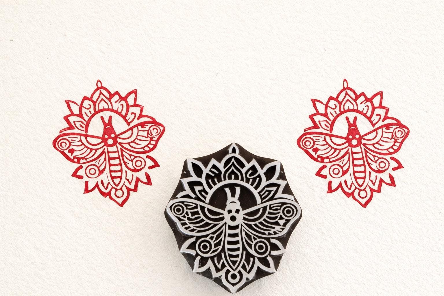 Hand-carved mandala moth stamp printing intricate symmetrical insect design on paper.