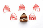 Beehive wooden block printing stamp creating red beehive prints on white paper with the carved stamp in the center.